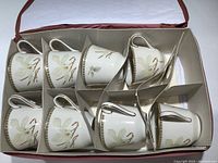 Eight white fine china cups and matching saucers with White Nile floral pattern and gold trim, neatly arranged inside pink padded case with dividers.