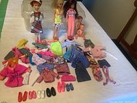 Wide view showing three dolls and two babies with a large variety of doll clothes and footwear spread on table