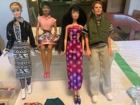 Three Barbie dolls and one Ken doll dressed in various outfits shown from front on a table