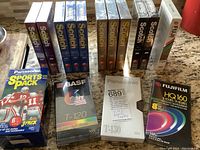 Overall view of 17 sealed blank VHS tapes laid out on counter including Scotch, BASF, Panasonic, Fujifilm, and Panasonic Sports Pack.