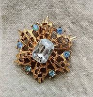 Close-up of gold-tone open-work brooch with central large clear rectangular rhinestone and six smaller blue rhinestones arranged around it