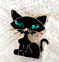 Front view of the black enamel cat brooch showing green rhinestone eyes and gold-tone metal detailing.
