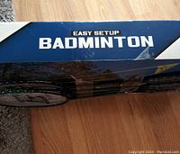 Photo of the closed original box with 'Easy Setup Badminton' label showing branding and partial view of replaced rackets inside.