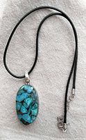 Full view of the turquoise and sterling silver pendant necklace lying flat on a fabric background showing the pendant and cord.