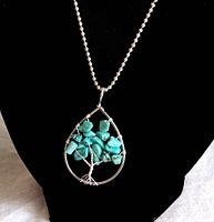 Full view of the pendant necklace on a black display, showing the treetop made of turquoise stones and sterling silver wire teardrop frame.