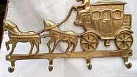 Close-up of bronze wall hanger showing detailed casting of horse-drawn coach with driver and horses and four hooks underneath.