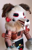 Front view showing detailed carved wolf mask with fur, leather arm bands, and colorful apron on wood base.