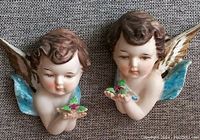 Both porcelain bisque angels displayed side by side showing facial details and flower offerings.