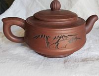 Side view of a reddish-brown Yi-Xing Zisha teapot showing hand-etched bamboo design on the body