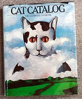 Front cover of a large vintage hard-cover cat book titled 'Cat Catalog: The Ultimate Cat Book' featuring an illustrated cat emerging from clouds.