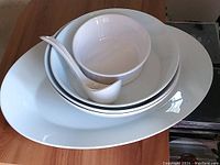Set of white porcelain serving pieces including platter, bowls, ladle, and baking dish seen stacked on table.