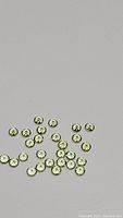 Top-down view of 38 small, round, faceted apple green peridot gemstones scattered on a gray surface, showing their size and color.