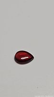 Pear-shaped deep cherry red garnet cabochon gemstone with smooth polished surface on white background.