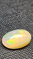 Close-up photo of natural oval cabochon Ethiopian opal on dark textured background showing play of color and smooth polished finish.