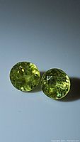 Pair of round cut sphene gemstones showing yellow-green color, strong luster and internal clarity features on white background.