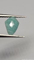 Close view of the shield-cut Amazonite gemstone held by tweezers, showing its robin's egg blue color and faceted faces.