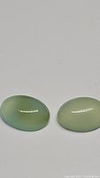 Close-up of the two oval cabochon chalcedony gemstones on a white background, showing their color and shape.