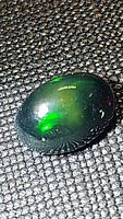 Oval cabochon Ethiopian black opal gemstone showing green play of color on jet black base