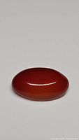 Oval polished cabochon natural fire red orange carnelian gemstone lying flat, showing smooth surface and rich deep red-orange color.