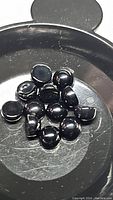 Multiple polished round cabochon jet black onyx gemstones approx 4mm on a black tray, showing smooth, glossy surface and uniform sizing.