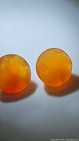Close-up image of two round faceted mandarin orange carnelian gemstones, showing their translucent orange color and surface detail.