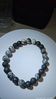 Clear view of the round beads on a stretchy bracelet laid on white circular surface, alternating black web jasper and black lava stone beads.