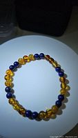 Photo of natural Baltic amber and Lapis Lazuli bead stretchy bracelet laid flat in a circular shape on white surface with dark background.