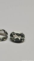 Close-up photo of two oval cut natural green amethyst gemstones with visible facets and light green color.