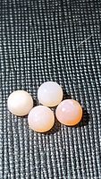 Four natural pink opal round cabochon gemstones on black textured fabric background, showing size and color differences