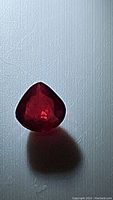 Close-up photo of the deep red, teardrop-shaped ruby showing its rich color and faceting.