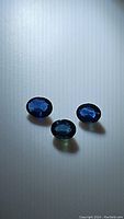 Three oval cut deep intense blue sapphires arranged on a light surface.