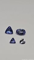Four natural tanzanite gemstones laid out on a neutral surface showing their color and cut variety.