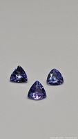 Three natural tanzanite stones, trillion cut, arranged in triangle, showing blue-purple strong color and good clarity.