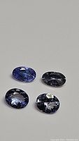 Four oval cut natural tanzanite gemstones in blue and purple hues arranged on a plain background.