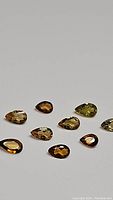 Photo showing ten pear-shaped faceted tourmaline gemstones in varying orange to yellow shades arranged on white background.