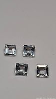 Four square-cut natural aquamarine gemstones on a plain surface, showing consistency in cut and clarity.