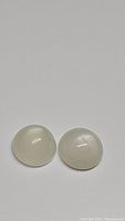 Two natural round cabochon white moonstones side by side on a gray background showing their smooth domed surfaces and flash effect observed on one stone.