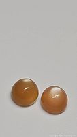Two round cabochon peach moonstones of deep peach color and high flash placed on a neutral background.