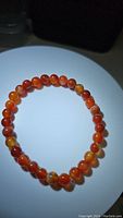 Top view of a stretchy bracelet composed of round, polished natural red agate beads with warm reddish-orange coloration and natural pattern variations on a white background.
