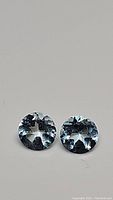 Close-up photo of round brilliant cut matched pair of sky blue topaz gemstones showing light blue color and facet details
