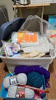 Photo of resin storage tote filled with white and purple wool yarn, batting, fabric, thread, and needles