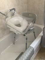 Adjustable shower chair with white padded seat lift covered in clear plastic, positioned in bathtub