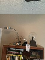 Photo showing the modern desk lamp and two plasma balls placed on a wooden bookshelf surrounded by books and papers.