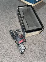 Top angled view of black and red model locomotive with its original protective foam box beside it.