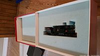 Open red and white cardboard box showing pale blue foam insert with locomotive model inside