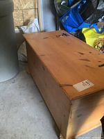 Top angle showing the rectangular pine blanket box with metal hinges and natural wood finish, along with scratches and wear.