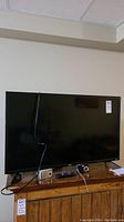 40 inch RCA Roku TV on wooden stand with power cord and two digital cameras placed in front.