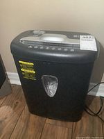 Front view of black Amazon Basics paper shredder, showing the front waste bin with transparent window and the main unit body.