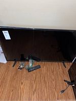 RCA 42 inch television with two legs, remote control on floor in front, and mounting hardware grouped to the side against a plain wall.