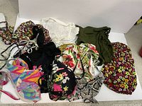 Photo showing 11 items: assorted bikini tops and bottoms with floral prints, colorful geometric, snake skin pattern, solid black, and one olive green bathing suit cover up with side drawstrings.